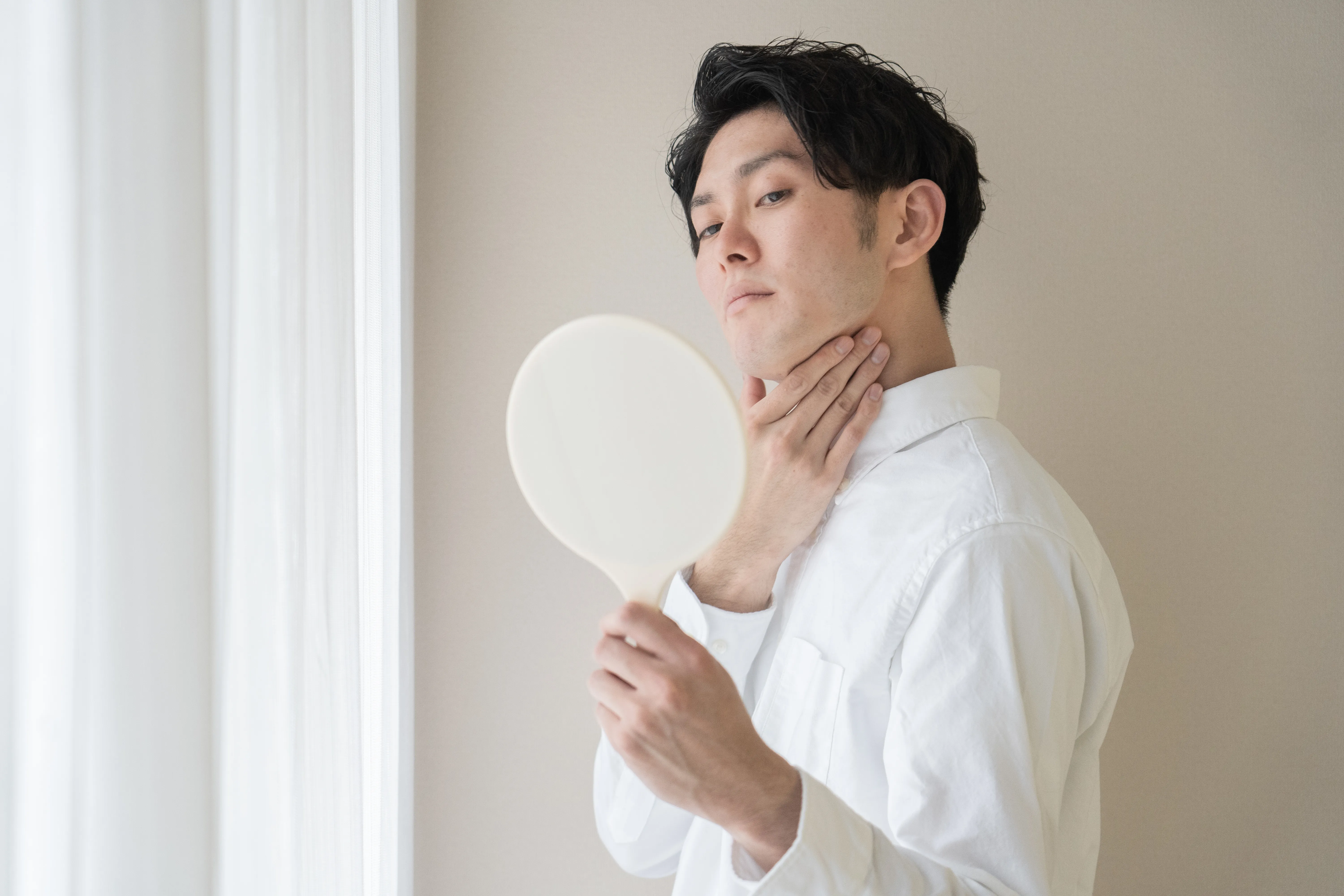 手鏡で自分の顎まわりの肌を確認している男性