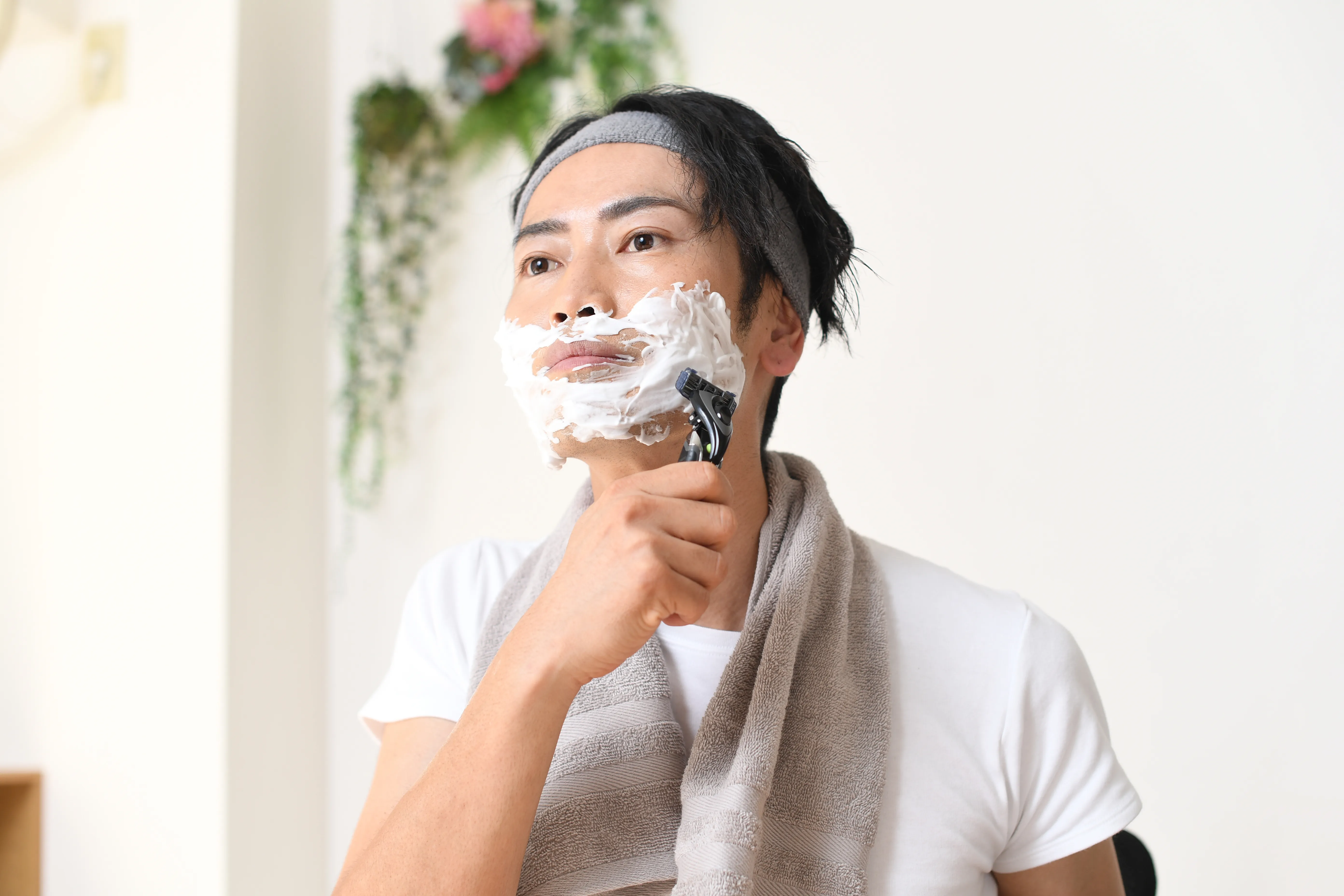 洗面所でシェービングフォームをつけてヒゲをそっている男性